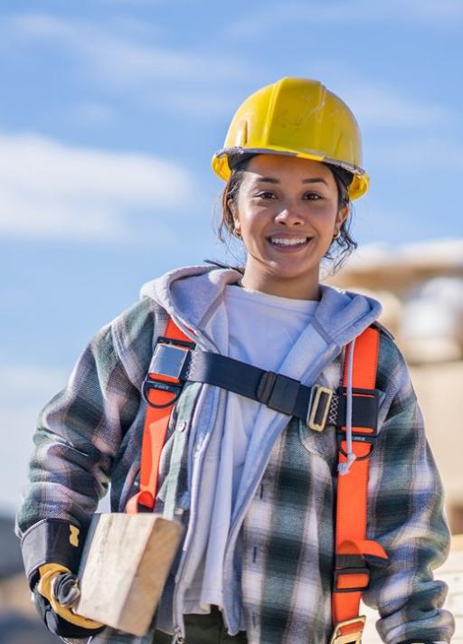 Femme ouvrière souriant, portant une planche en bois dans sa main droite